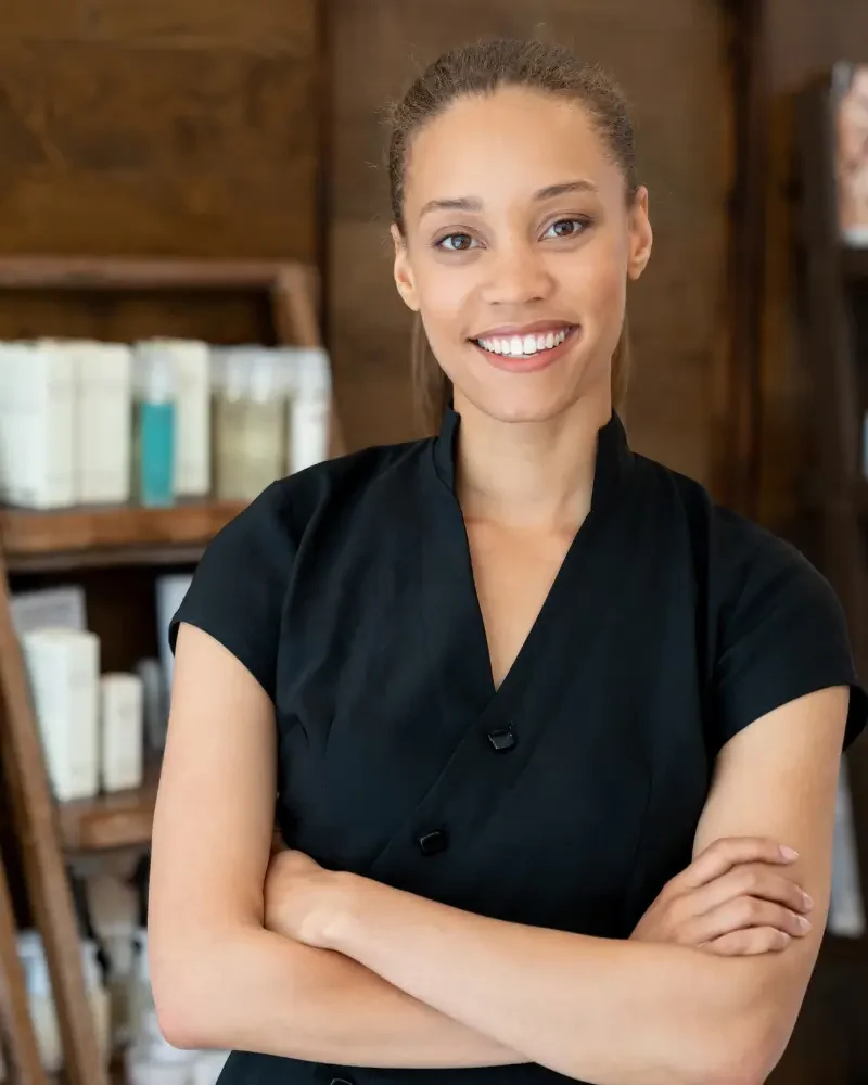 black woman with arms crossed standing in front of skincare products on shelf the maven method esthetician training