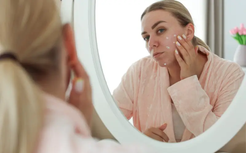 woman looking in the mirror at Menopause acne caused by hormonal changes, inflammation, and skin barrier disruption