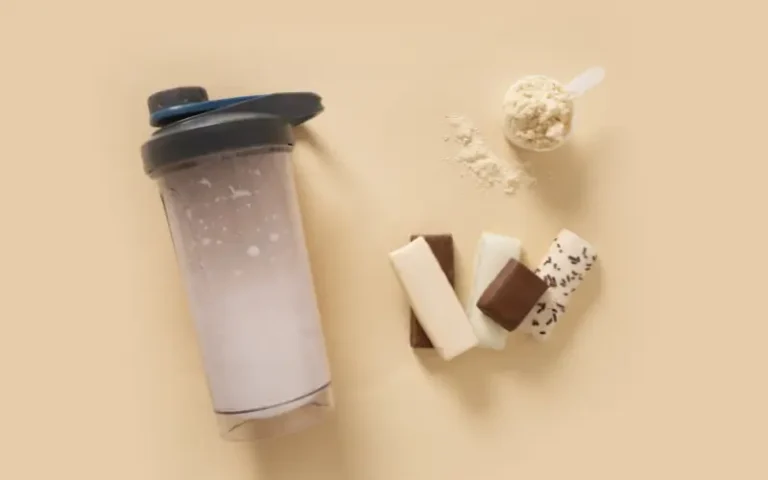 Protein shaker bottle, scoop of powder and protein bar arranged on a neutral background, representing acne safe protein choices.