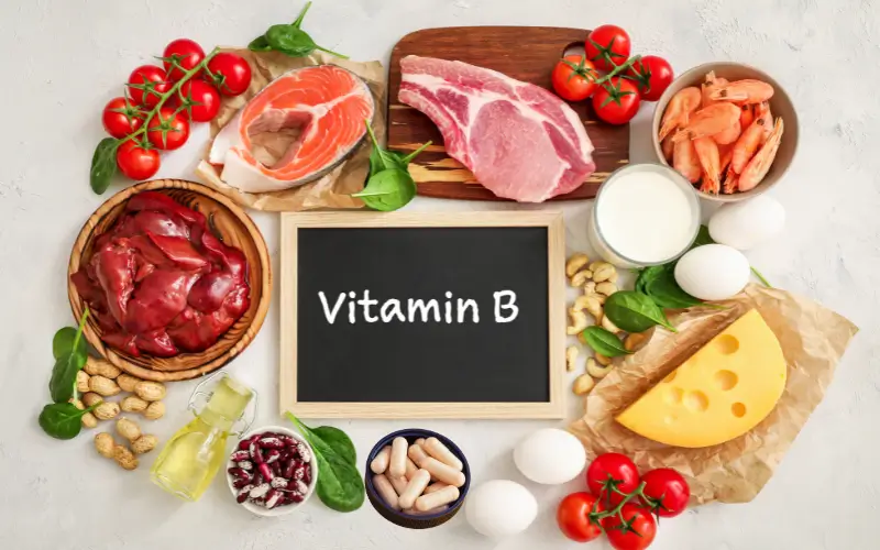 Assorted B vitamin capsules and bottles arranged with leafy greens on a neutral background, representing the connection between B vitamins and acne.