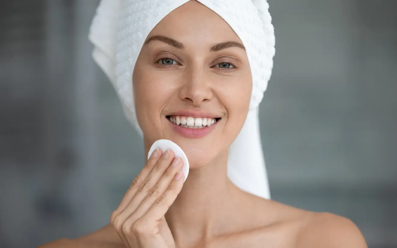 woman with towl on hair applying skincare acid with a cotton pad