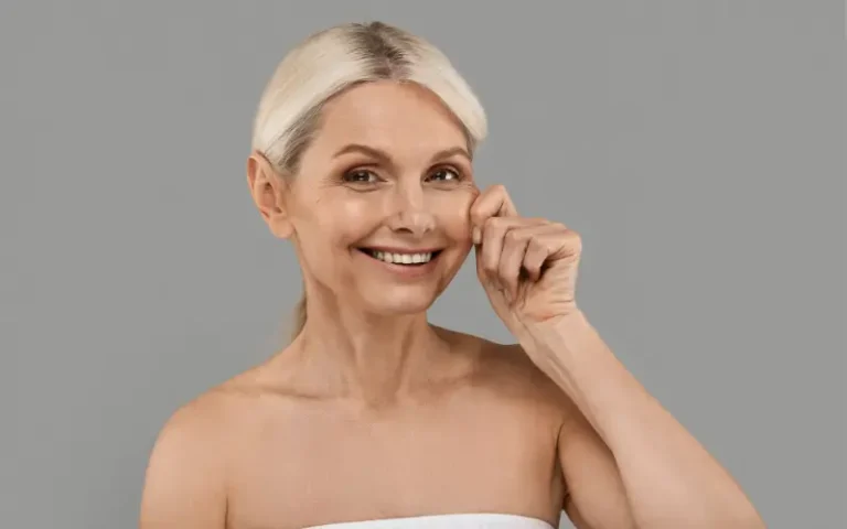 mid-life woman pinching her own cheek with a smile to represent menopause weight changes and skin firmness changes