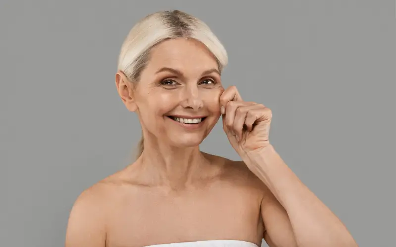 mid-life woman pinching her own cheek with a smile to represent menopause weight changes and skin firmness changes