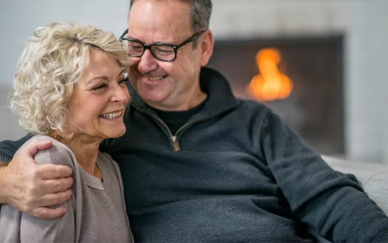 woman going through menopause sitting on the couch embraced by her supportive husband